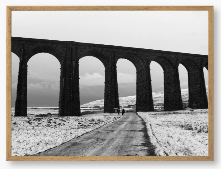 black and white Framed Photo of a Viaduct in a snowy landscape with people walking on a path below.