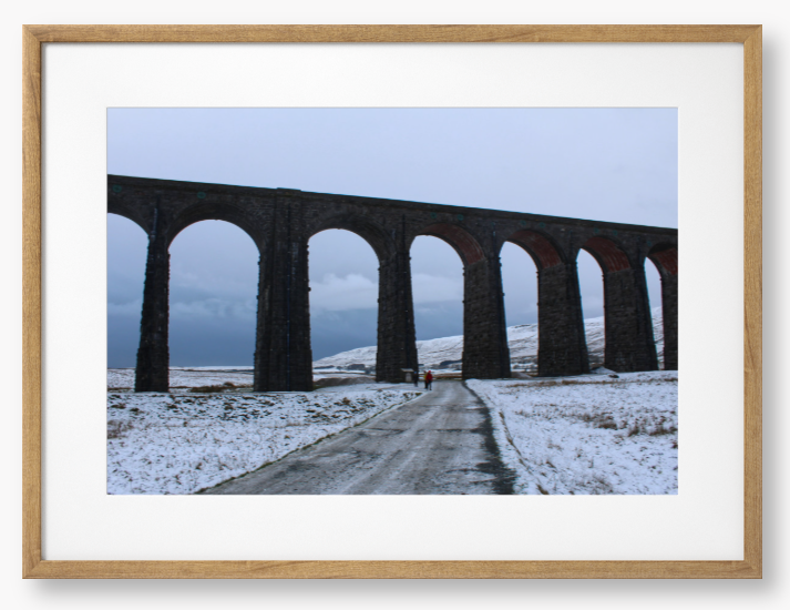 Framed Photo of a Viaduct in a snowy landscape with people walking on a path below.
