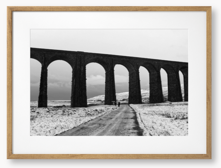black and white Framed Photo of a Viaduct in a snowy landscape with people walking on a path below.