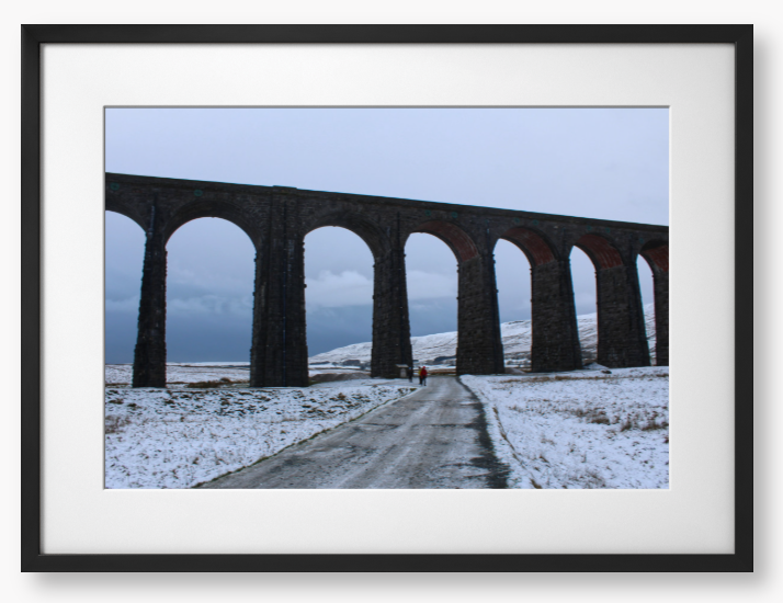 Framed Photo of a Viaduct in a snowy landscape with people walking on a path below.