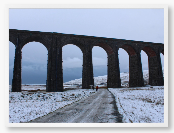 Framed Photo of a Viaduct in a snowy landscape with people walking on a path below.
