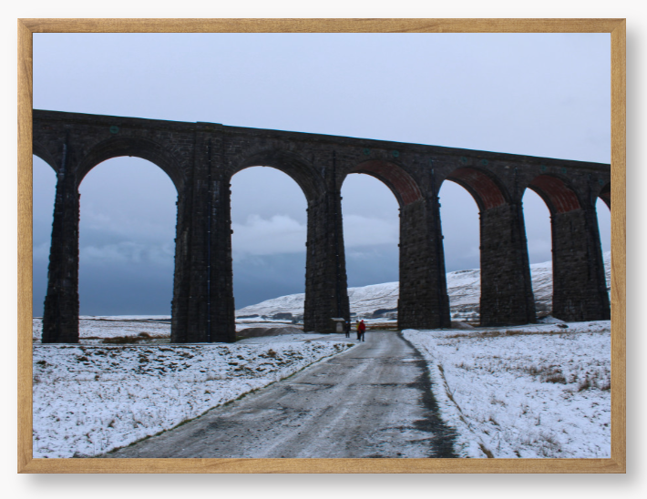 Framed Photo of a Viaduct in a snowy landscape with people walking on a path below.