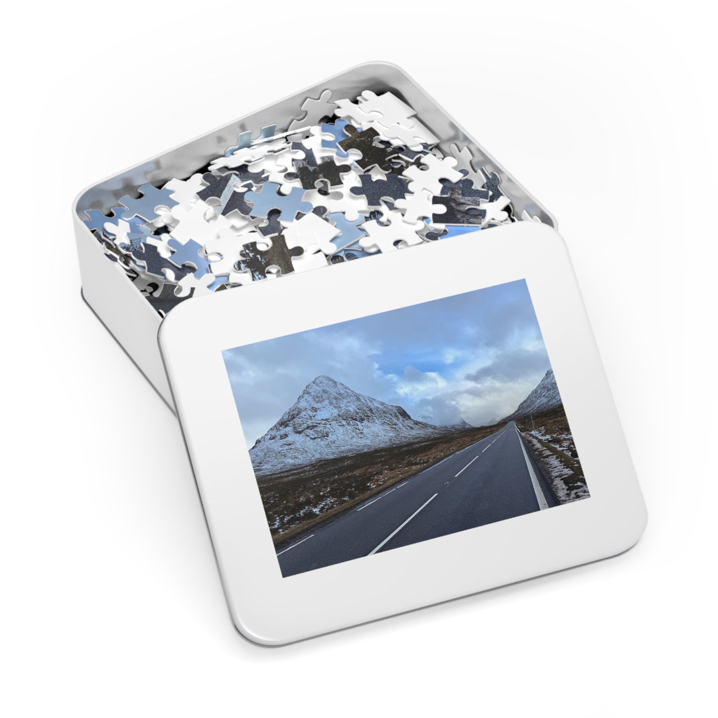 Jigsaw puzzle in a tin with a scenic road and mountain image on the lid.