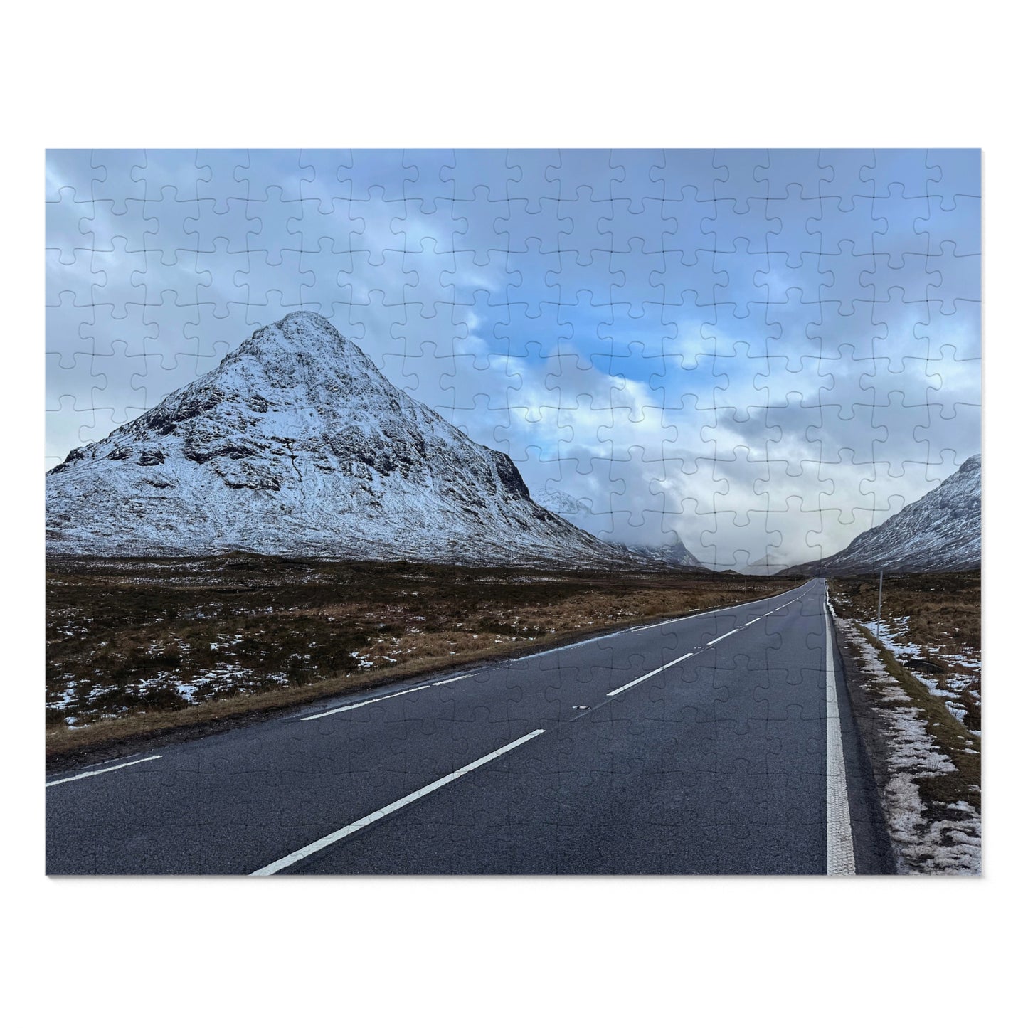 Road leading to snow-capped mountains under a cloudy sky