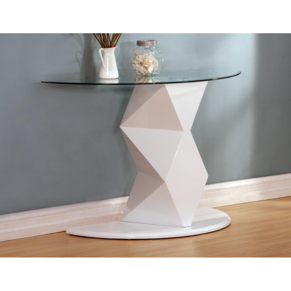 White high gloss console table with a geometric design, placed on a wood floor against a wall with a clear glass top and a decorative vase on top.