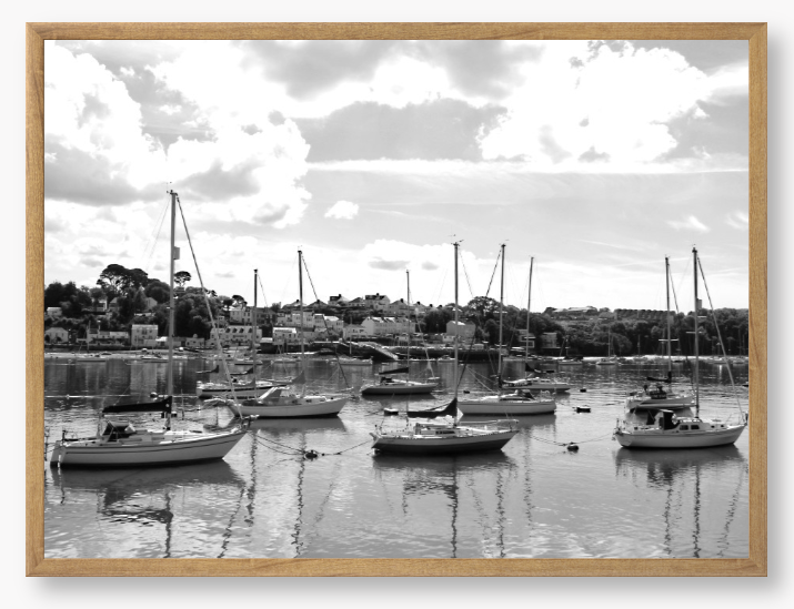 Black and white framed photograph of sailboats docked in a harbor with a cloudy sky.