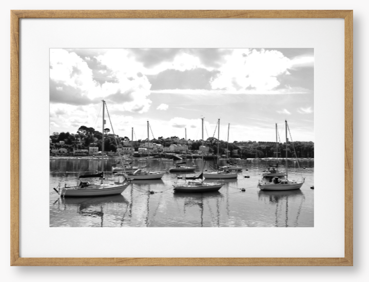 Black and white framed photograph of sailboats docked in a harbor with a cloudy sky.