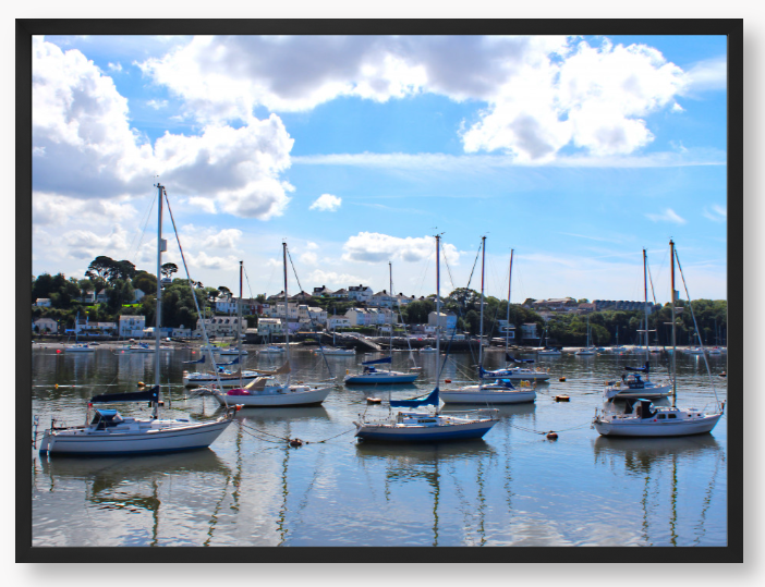 Framed Photo of a Harbour scene with boats docked in calm water under a blue sky with clouds.