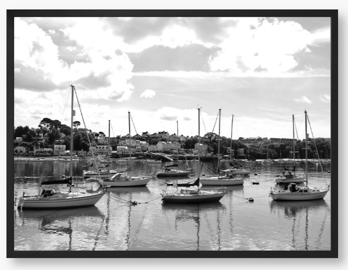Black and white framed photograph of sailboats docked in a harbor with a cloudy sky.