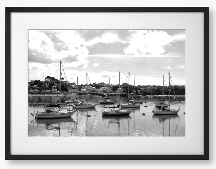 Black and white framed photograph of sailboats docked in a harbor with a cloudy sky.