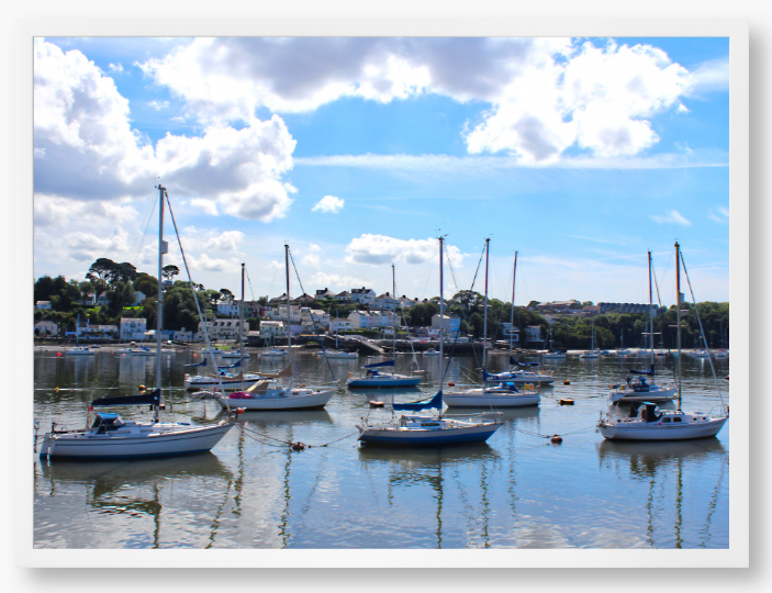 Framed Photo of a Harbour scene with boats docked in calm water under a blue sky with clouds.