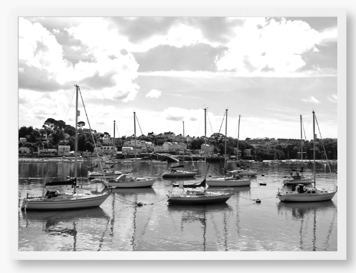 Black and white framed photograph of sailboats docked in a harbor with a cloudy sky.