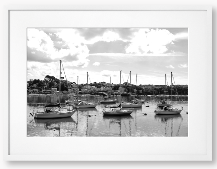 Black and white framed photograph of sailboats docked in a harbor with a cloudy sky.