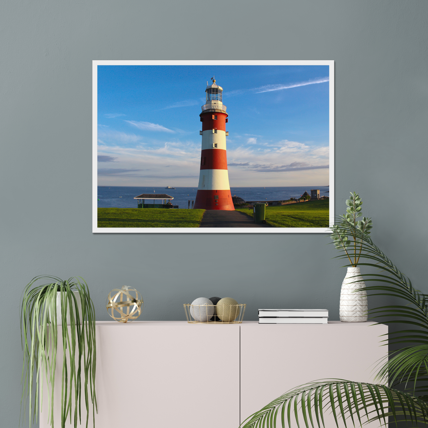 Framed picture of a lighthouse on a wall above a white cabinet with decorative items.