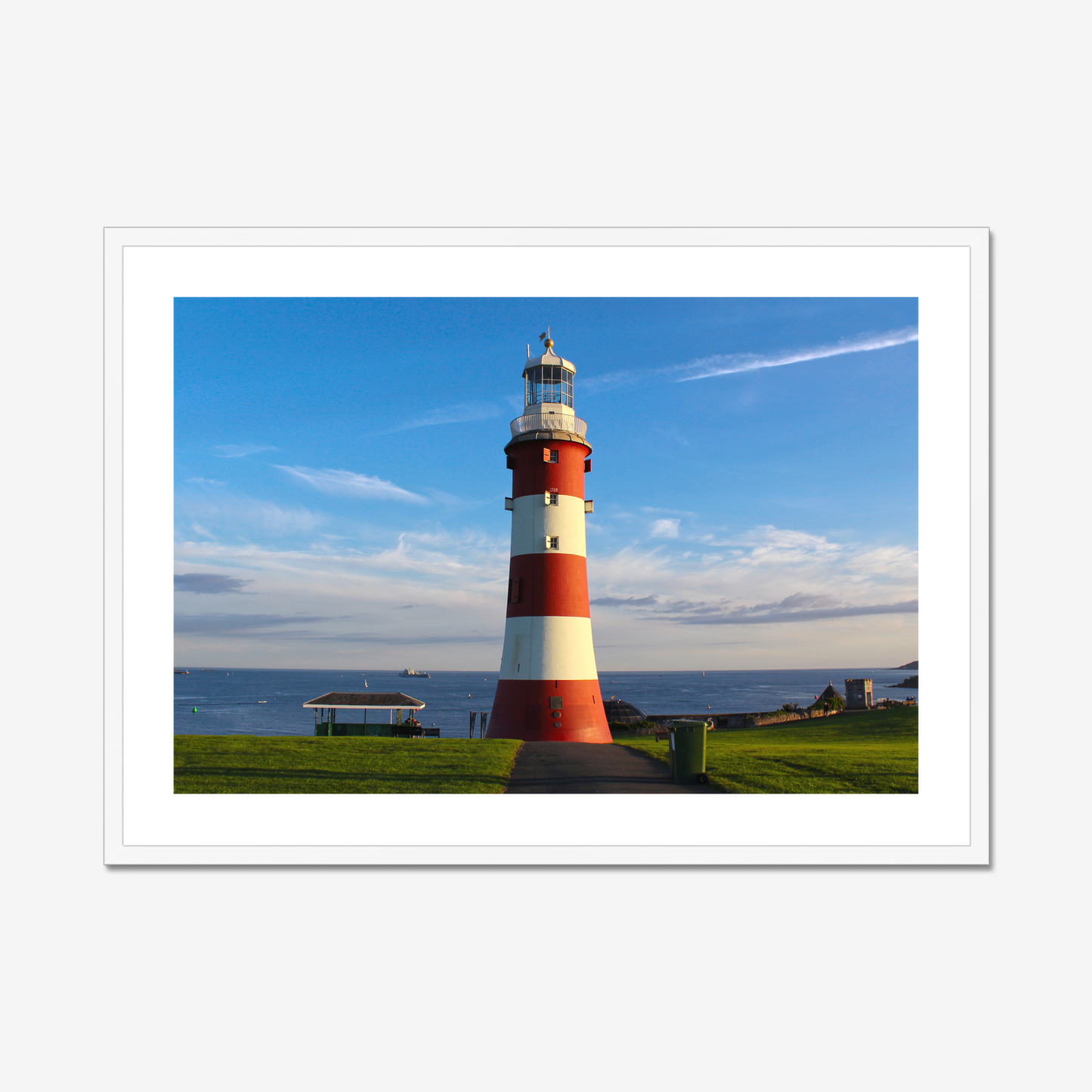 Red and white lighthouse on a grassy area with a blue sky background