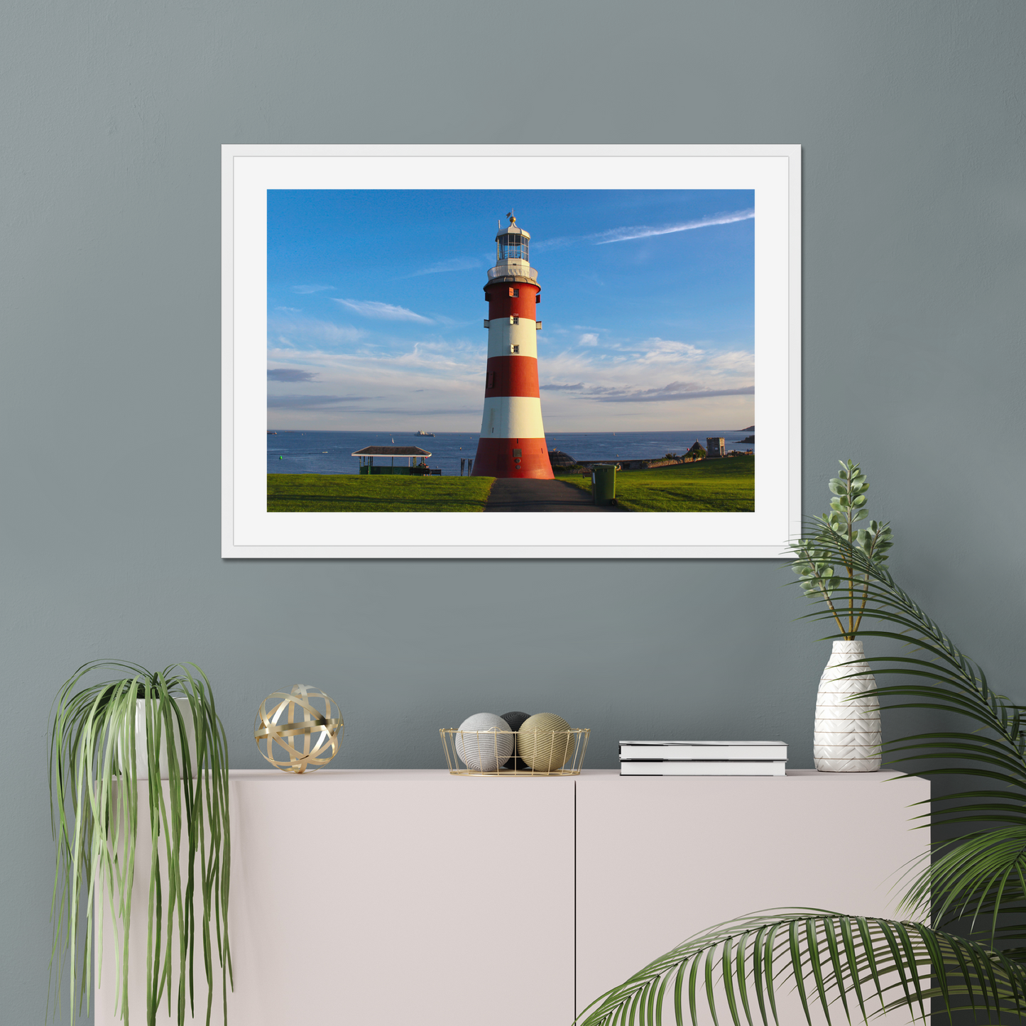 Framed picture of a lighthouse on a wall with decorative items below