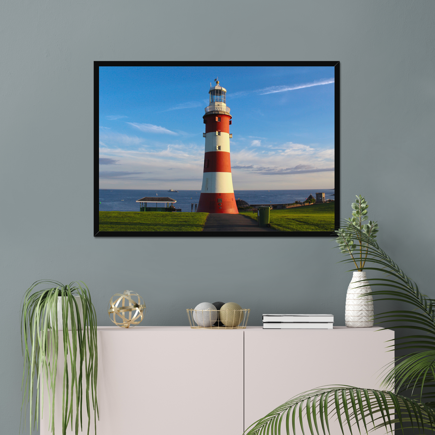 Framed picture of a lighthouse on a wall above a white cabinet with decorative items.