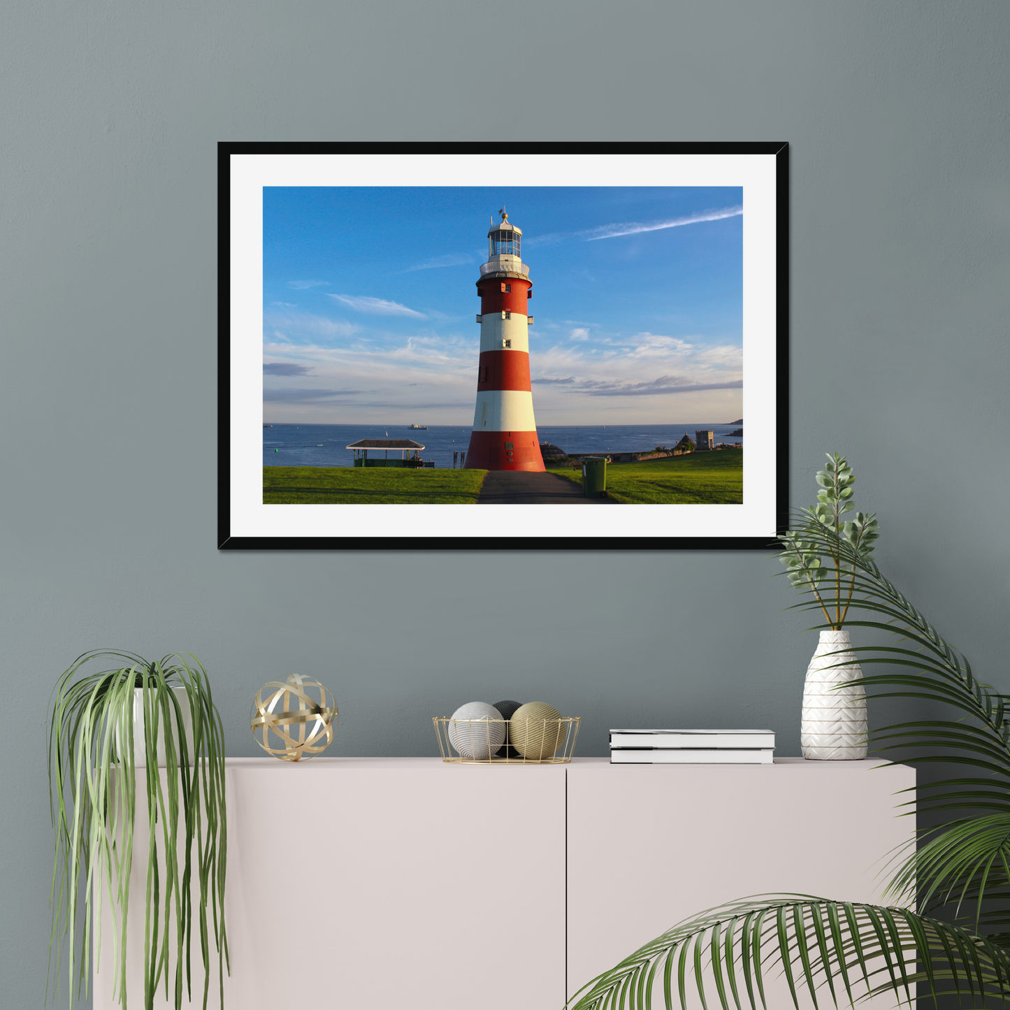 Framed picture of a lighthouse on a wall with decorative items below