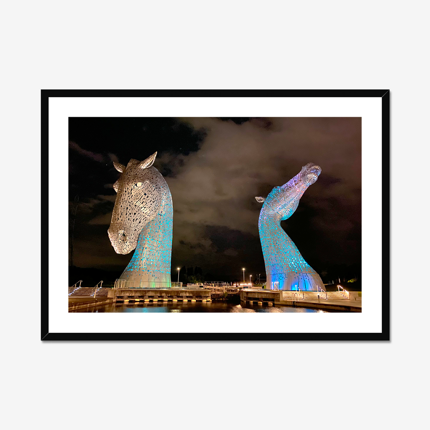Framed photograph of illuminated horse head sculptures against a dark sky.