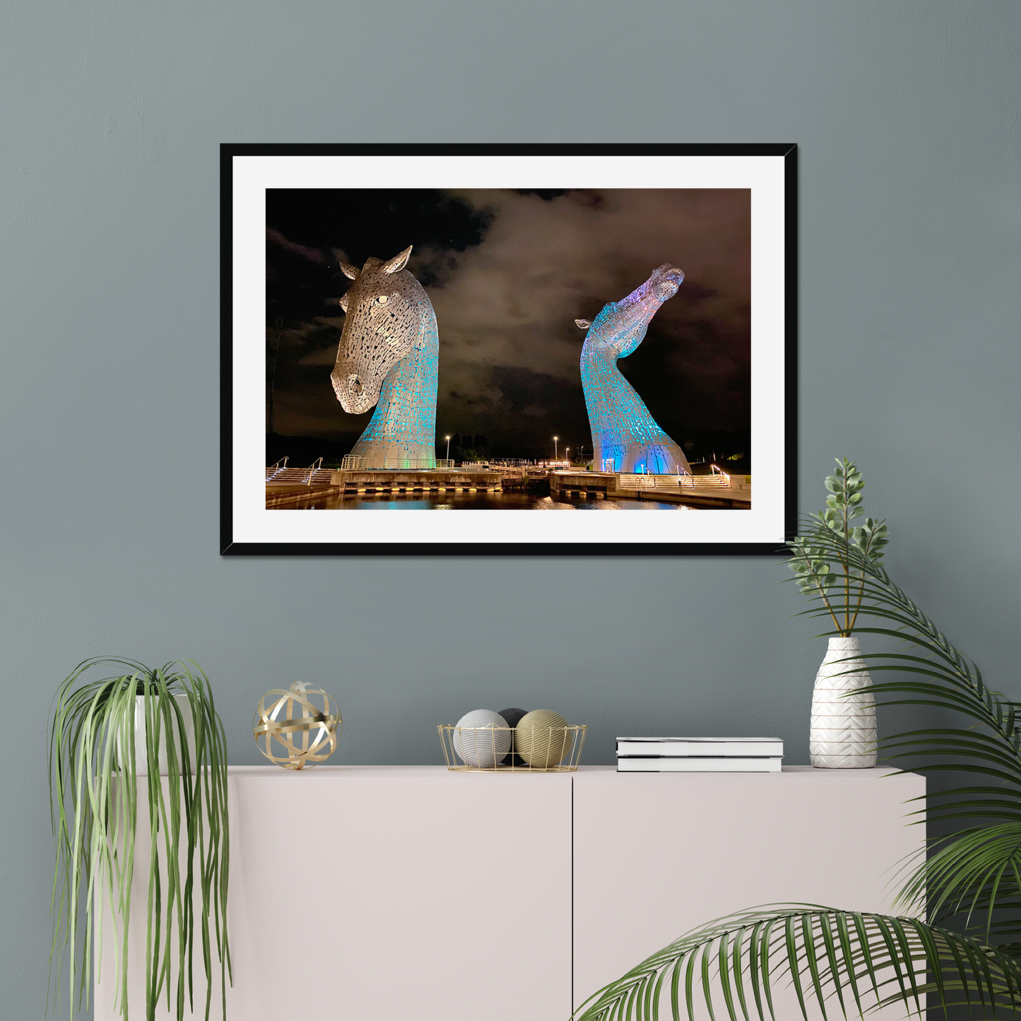 Framed artwork of illuminated horse sculptures on a wall above a cabinet with decorative items.