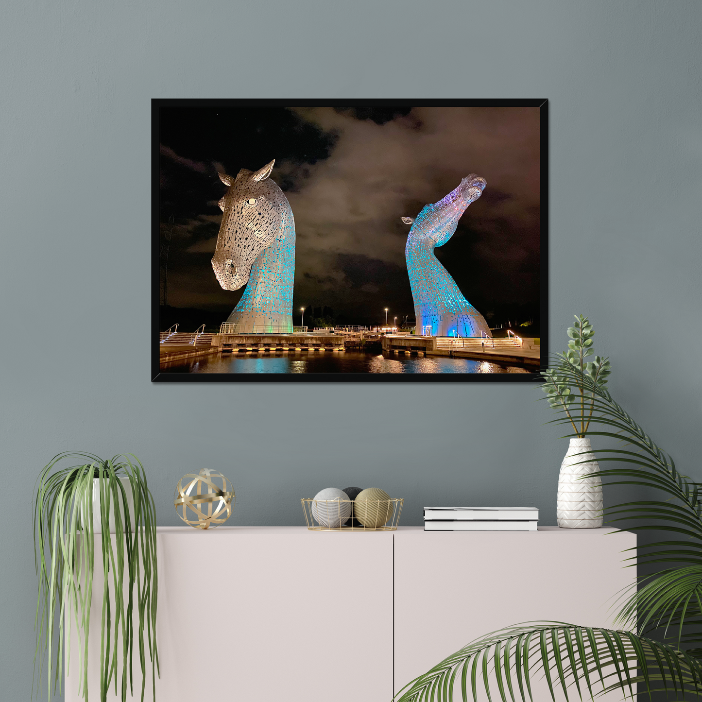 Framed artwork of illuminated horse sculptures on a wall above a cabinet with decorative items.