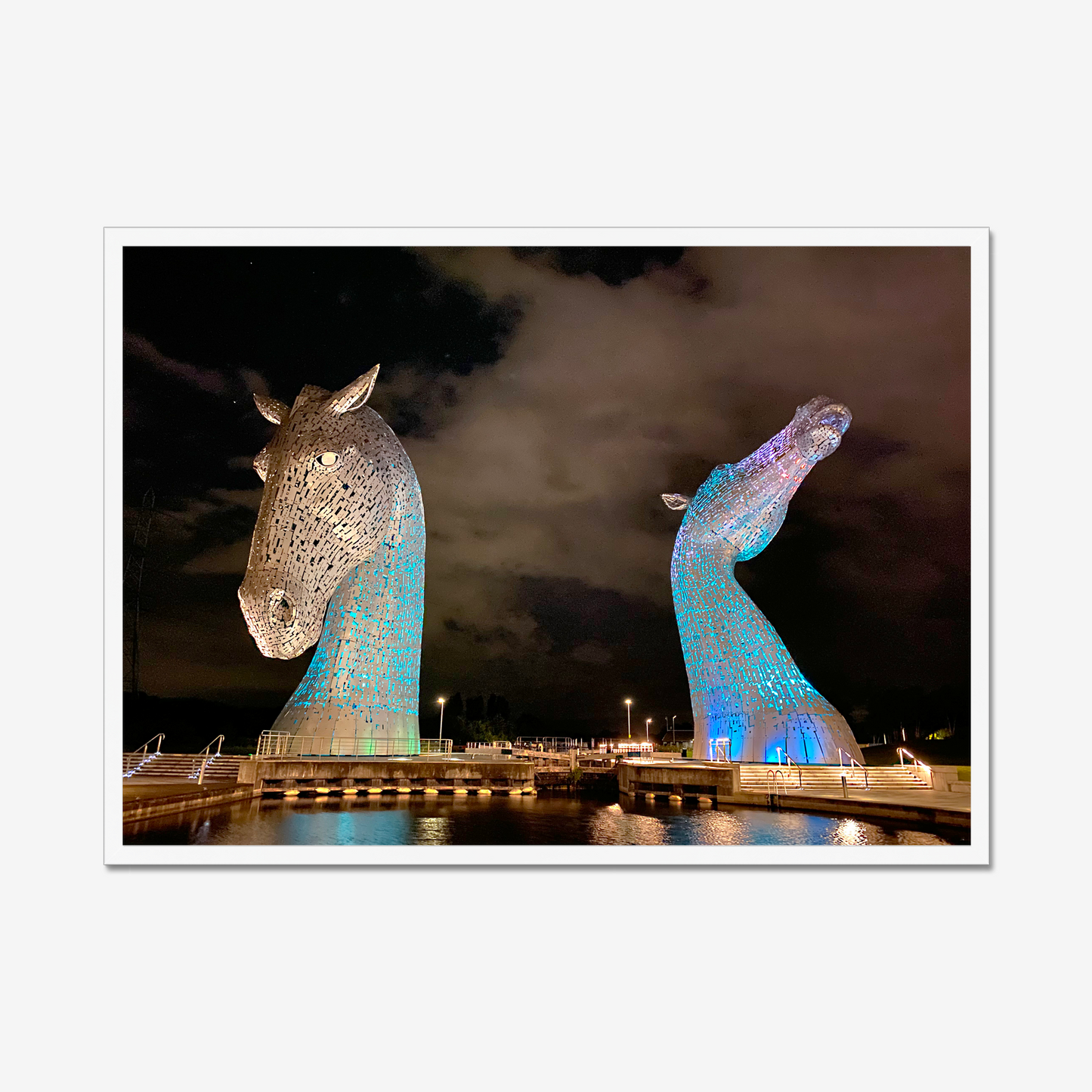 Two large horse head sculptures illuminated at night with a dark sky background.