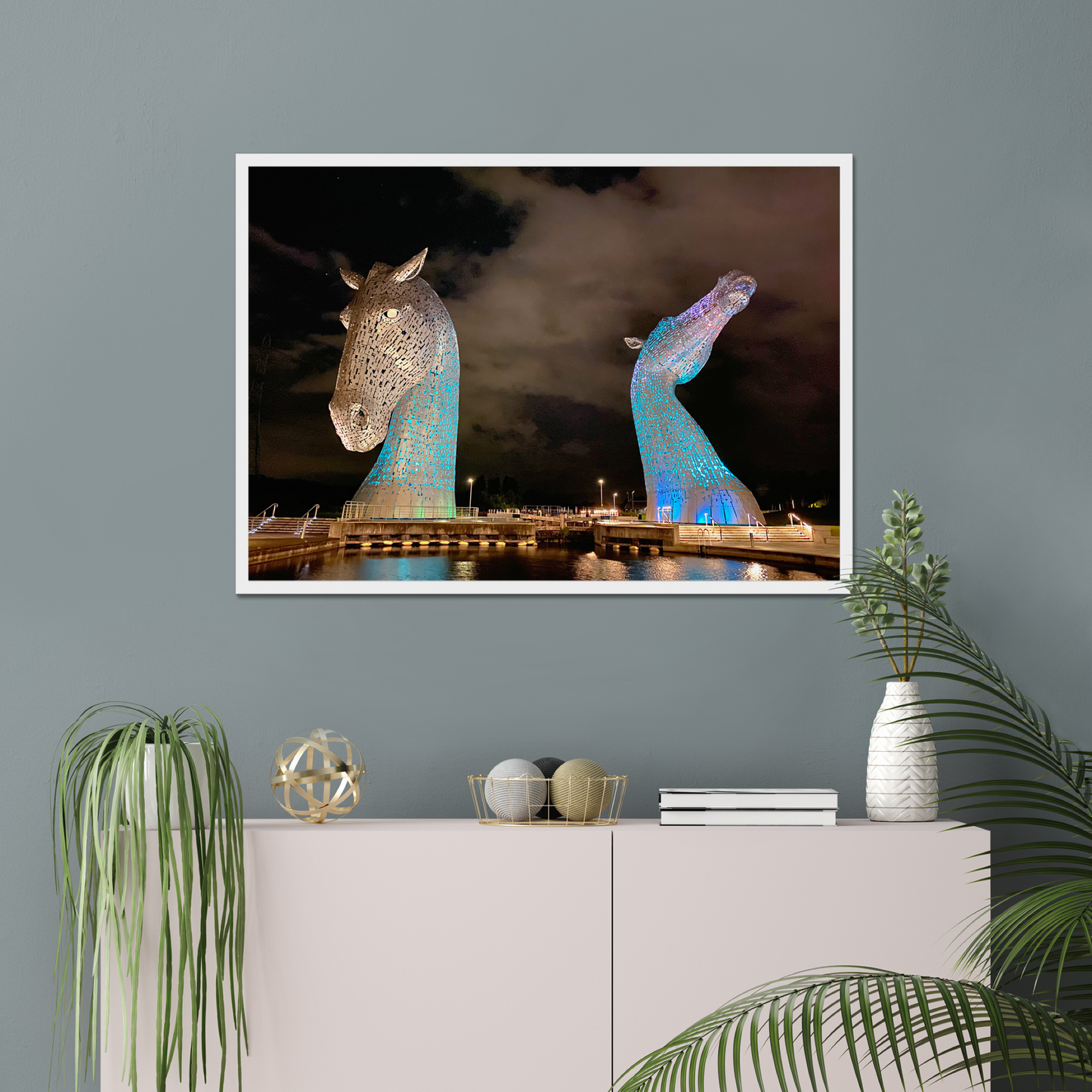 Framed artwork of illuminated horse sculptures on a wall above a cabinet with decorative items.