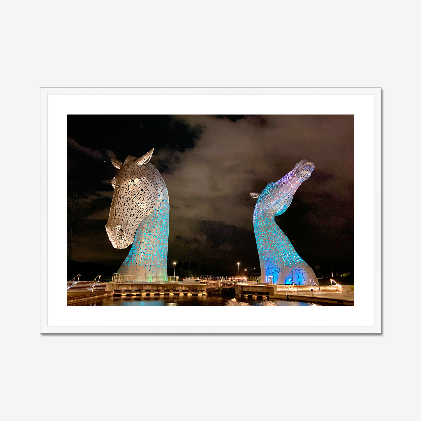 Two large horse head sculptures illuminated at night with a dark sky background.