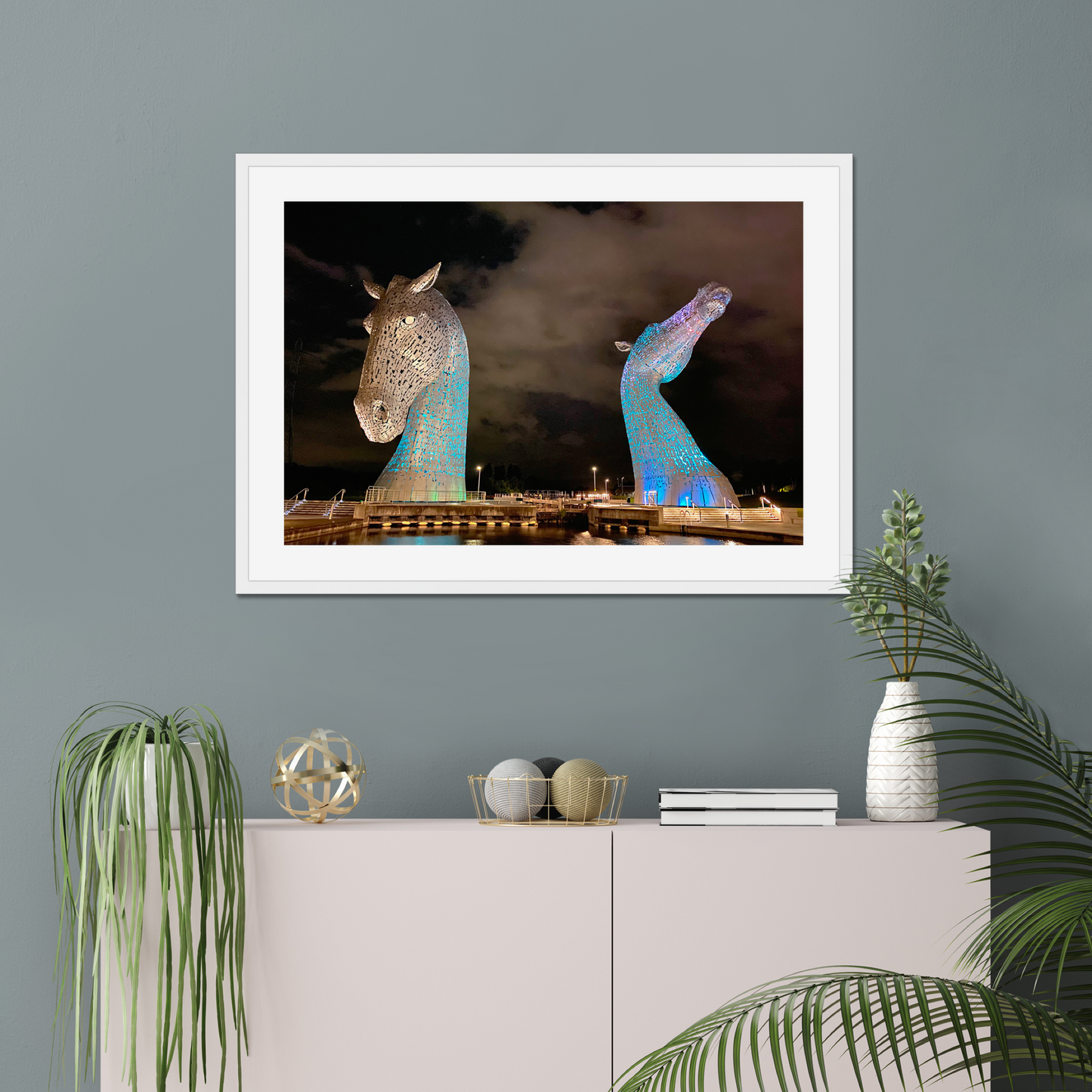Framed artwork of illuminated horse sculptures on a wall above a cabinet with decorative items.
