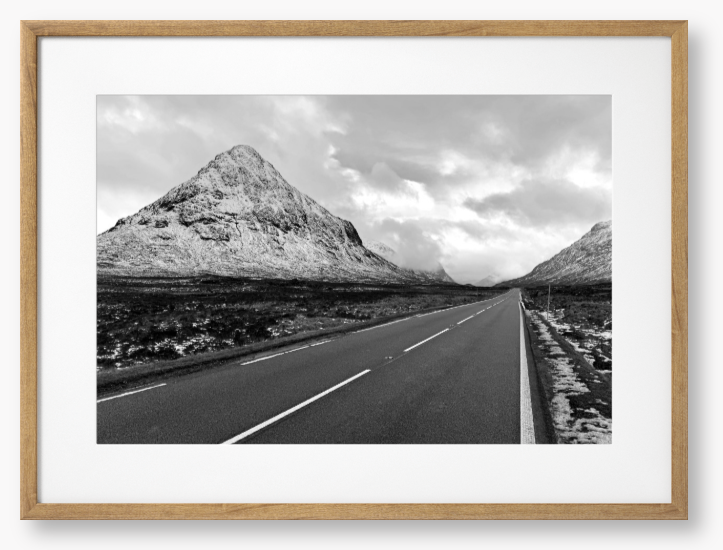 Black and White Framed Photo of a road leading towards snow-capped mountains under a cloudy sky