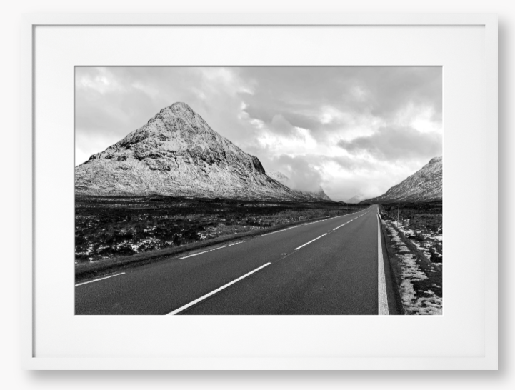 Black and White Framed Photo of a road leading towards snow-capped mountains under a cloudy sky