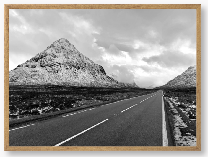 Black and White Framed Photo of a road leading towards snow-capped mountains under a cloudy sky