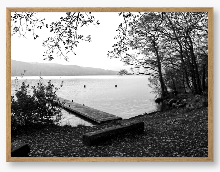 Black and white framed photo of a scene of a lake with a wooden jetty and trees.