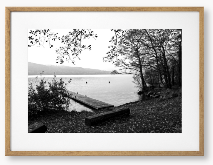 Black and white framed photo of a scene of a lake with a wooden jetty and trees.