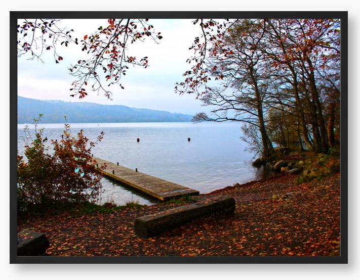 Framed Photo of a Autumn scene by a lake with a wooden jetty and trees with red leaves.