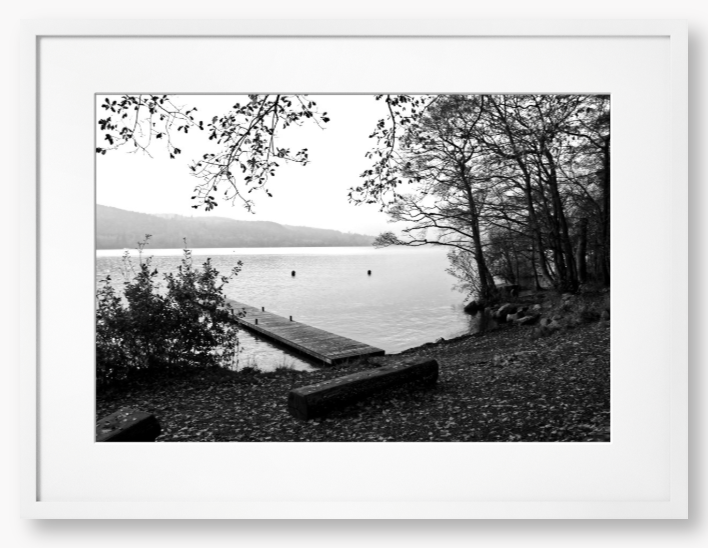 Black and white framed photo of a scene of a lake with a wooden jetty and trees.