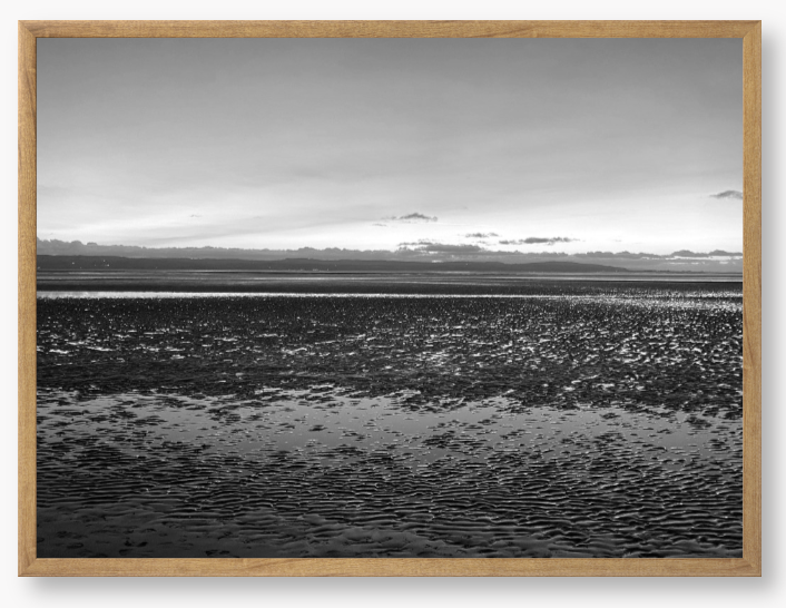 Black and white framed photo of a coastal scene with mountains in the distance.