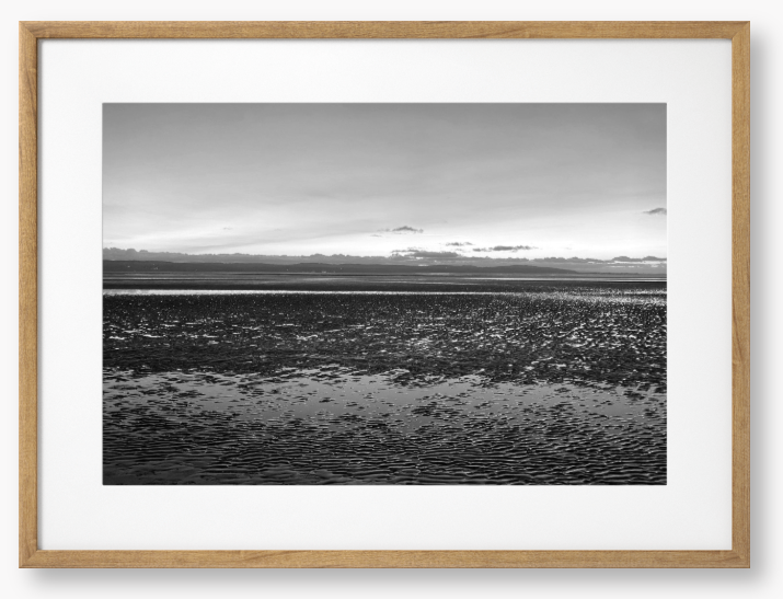Black and white framed photo of a coastal scene with mountains in the distance.