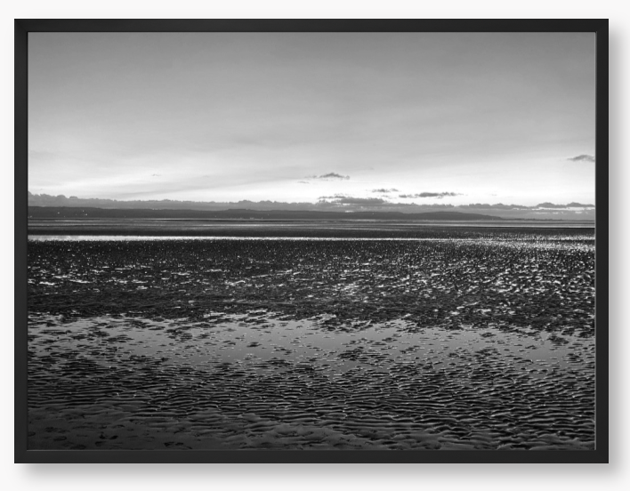 Black and white framed photo of a coastal scene with mountains in the distance.