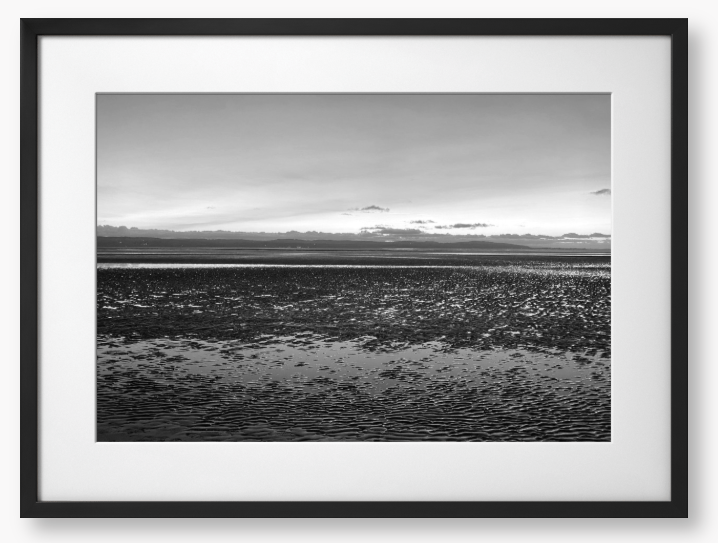 Black and white framed photo of a coastal scene with mountains in the distance.