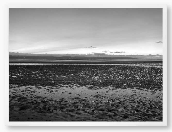 Black and white framed photo of a coastal scene with mountains in the distance.