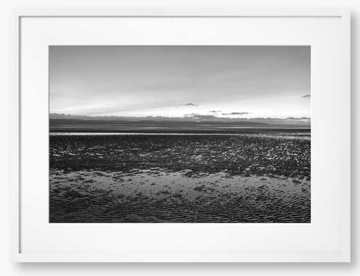 Black and white framed photo of a coastal scene with mountains in the distance.