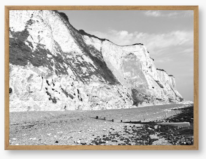 Black and white framed photograph of a coastal landscape with cliffs and beach.