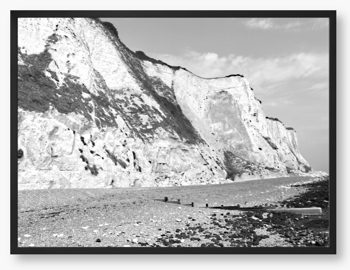 Black and white framed photograph of a coastal landscape with cliffs and beach.