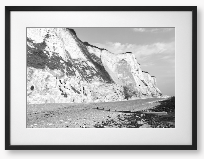 Black and white framed photograph of a coastal landscape with cliffs and beach.