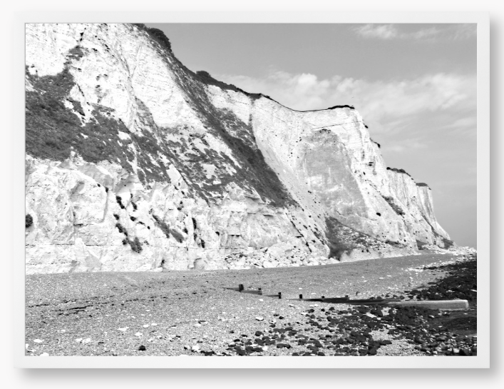 Black and white framed photograph of a coastal landscape with cliffs and beach.