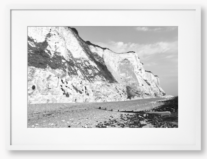 Black and white framed photograph of a coastal landscape with cliffs and beach.
