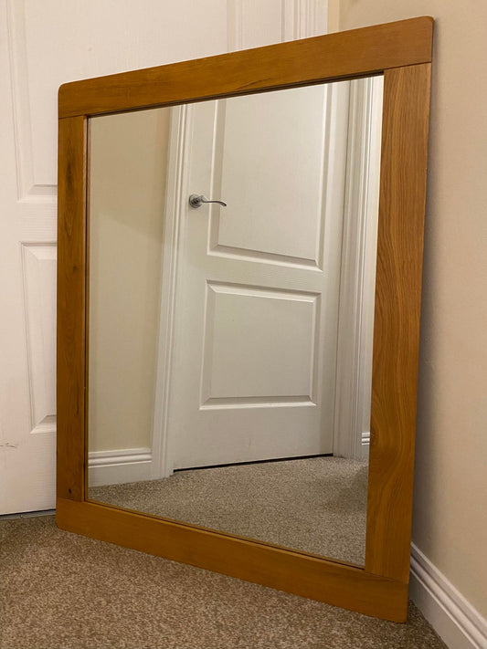 A large rectangular oak mirror leaning against a wall, reflecting a door and part of a room.