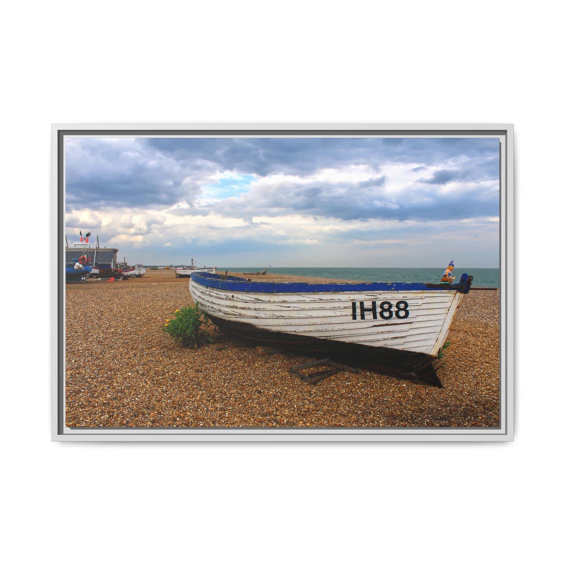 Framed photograph of a boat on a pebble beach with a cloudy sky.