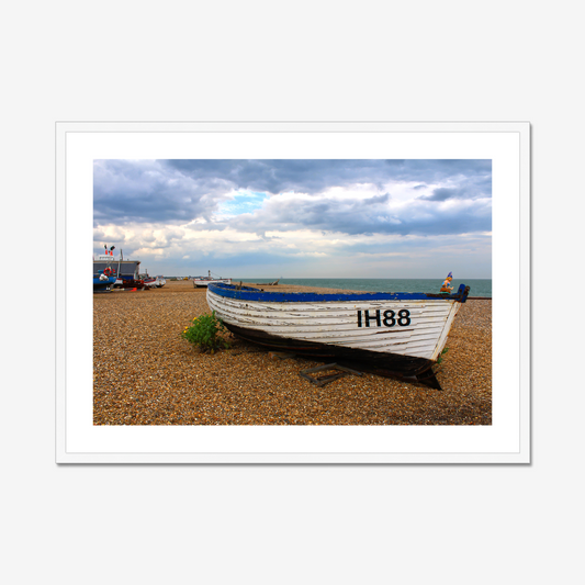 Framed photograph of a boat on a pebbly beach with a cloudy sky.